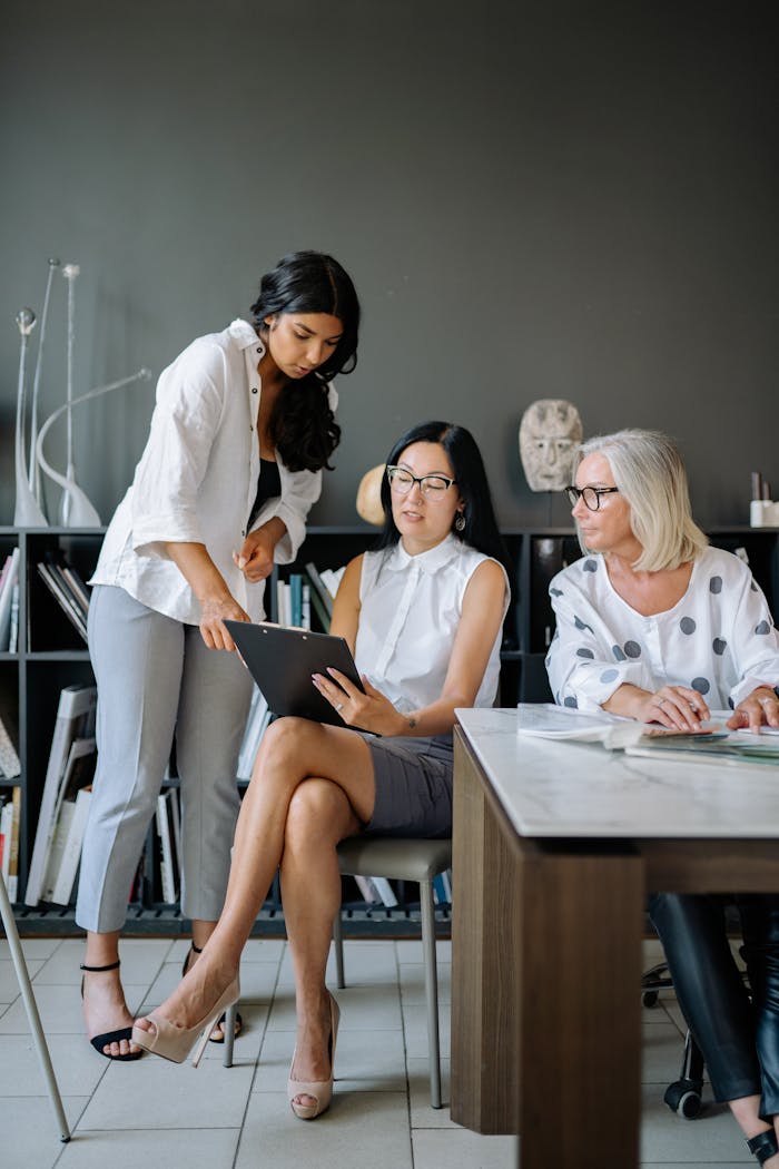 Three professional women engaged in a collaborative discussion in a modern office environment.